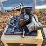 A detailed view of the bronze still-life sculpture honoring Jim Saad, showcasing his cobbler's tools and a boot placed on a sandstone pedestal, symbolizing the craftmanship and history of his trade.