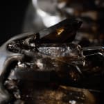 Close-up of the smoky quartz crystals embedded in the back of the sculpture. The photo captures the raw, jagged texture of the crystals contrasted against the sleek, polished aluminum surface, emphasizing the interplay of materials.