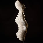 Front view of a bronze sculpture with a rippled spine of clear quartz crystals by James Lomax. The figure stands upright on a metal base, with the smooth bronze contrasting against the rough natural texture of the quartz.