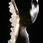 Another close-up of the sculpture's profile, capturing the light as it interacts with the clear quartz crystals and the polished bronze, creating a play of light and shadow that emphasizes the figure’s contemplative pose.