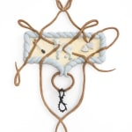 A small plaster wall relief sculpture by Erica Westenberger. The central composition includes an unlit match, a lamb, and two small hearts. Wood carved to look like rope or string twists around the three figures in loops.