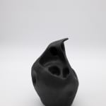 An abstract ceramic sculpture by Emily DiPalo in the shape of a black ghost. The top is pointed and there are random holes throughout.