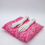 A ceramic sculpture by Christian Dinh of two white ceramic hands with a french manicure on a pink pillow.
