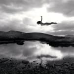 Silver gelatin print of Slate Gray Gallery artist Jerry Uelsmann's "Untitled, 1987 (Flying Figure Colorado) of a woman flying over a lake with mountains in the background in black and white