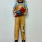 Slate Gray Gallery Artist Julie McNair's clay and oil sculpture of a gardener wearing yellow overalls with a vine on the left leg holding a red pepper titled "pick a pepper"