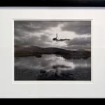 Silver gelatin print of Slate Gray Gallery artist Jerry Uelsmann's "Untitled, 1987 (Flying Figure Colorado) of a woman flying over a lake with mountains in the background in black and white