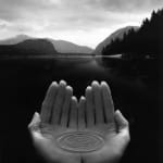Silver Gelatin Print of hands holding water in front of a mountain landscape by Fringe Gallery artist Jerry Uelsmann