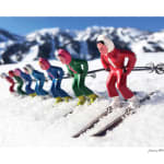 a color photograph of seven female skiers in colorful outfits posed to ski downhill