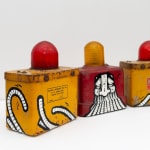 Two yellow with red light on top and a red with yellow light on top antique emergency road lights with GATS character painted across the three lights in black and white