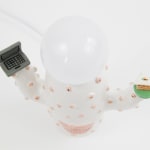 aerial view of Jen Dwyer lamp sculpture of white cactus with pink lips holding laptop and slice of cake. Lightbulb sits on top