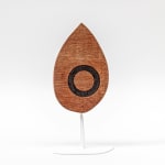 Wooden sculpture of a tear drop shaped wooden piece with a black circle on a white steal stand