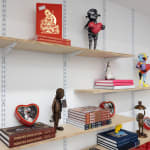 wooden shelves on a white wall with objects like books and robot sculptures on them