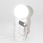 side of Jen Dwyer lamp sculpture of white cactus with pink lips holding laptop and slice of cake. Lightbulb sits on top