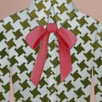 painting of a woman wearing a white and green patterned button up shirt, with a pink bow by Angela Burson