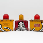 Two yellow with red light on top and a red with yellow light on top antique emergency road lights with GATS character painted across the three lights in black and white