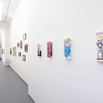 gallery hallway with white walls with numerous colorful pieces by Chris RWK and an inflatable robot installation in the background