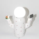 back of Jen Dwyer lamp sculpture of white cactus with pink lips holding laptop and slice of cake. Lightbulb sits on top