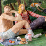 Scenic sculpture of a group of people sitting in a park under palm trees eating in n out on the grass.
