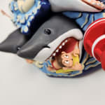 sculpture of a multiple shark heads, humans, and boats coming out towards the viewer