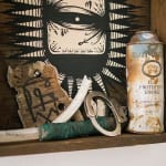 Wooden shelf with painting of an eye by GATS with several trinkets in the shelf including a spray can, handcuffs, piece of wood and a knife