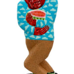 Sculpture of a man riding a skateboard holding a cut open watermelon. There are two different but similar sides. This side of his face are red and he is wearing a blue sweater with light blue clouds on it. There is a red beanie on his head.