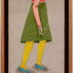 Embroidered figure holding a cigarette, wearing a knee length green skirt and a pink long sleeve top with blue flat shoes.