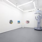 wide shot image of a gallery with paintings on the walls and a large inflatable robot in the back right corner
