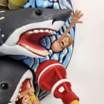sculpture of a multiple shark heads, humans, and boats coming out towards the viewer