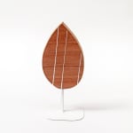Wooden sculpture of a tear drop shaped piece of wood with three white stripes vertically across it on a white steal stand