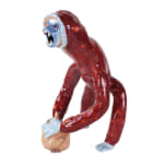 Ceramic sculpture of a monkey with red spots, a blue face, hands and feet, holding a large onion.