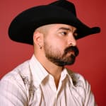Photo of a man with a beard wearing a black cowboy hat and a white shirt on a red background