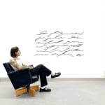 Man sitting next to Black scribble artwork from Arnaud Vidricaire resembling an abstract text paragraph made of laser cut burnt wood