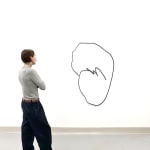 Man standing next to Black scribble abstract work from Arnaud Vidricaire in the shape of an imperfect circle with a scribble going through the middle made of laser cut burnt wood