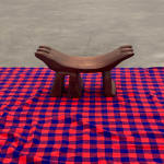 A curved wooden headrest with three divisions on either side and three legs on a red and blue patterned cloth
