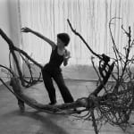 An artist dancing in a pose that parallels the shape of her sculpture