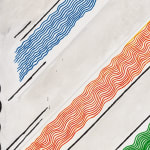 Detail image of a white and gray painting with diagonal lines in blue, orange, and green, jagged black marks around the top, left, and bottom of the canvas with a jumble of black lines on the right hand side.
