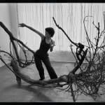 An artist dancing in a pose that parallels the shape of her sculpture