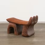 A wooden headrest with three finger-like shapes curving up on one side and three legs