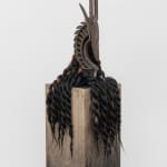 Carving of a wooden gazelle head surrounded by locks of flowing dark hair on a pedestal