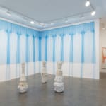 An installation view of gigantic cascading blue dresses on the wall over three ceramic sculptures on the floor