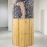 Round freestanding wood sculpture with an image of a male figure adhered to the surface and obscured by thousands of clear push pins