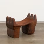 A wooden headrest with thick, stout legs and three finger-like rounded divisions curving up on either side