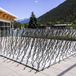 Rows of wire rope reach skyward in a wavy grid in front of an alpine landscape, casting shadows on the ground
