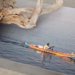 Karyn Olivier's, a close up view of a sculpture with a piece of drift wood sitting on top of a steel platform with a photograph of a man in a kayak in the water