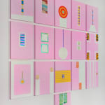 An array of colorful paintings comprised of geometric abstract forms displayed on a white wall