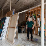 An artist, Carmen Cicero, standing amidst large-scale paintings in an industrial loft setting