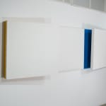 Detail of Tridimensional painting of 3 interconnected white flattened cubes. At the left one has a color strip in yellow, at the right, blue.