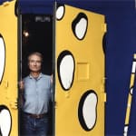 Photograph of Roy Lichtenstein opening double doors painted yellow with white spots outlined with black