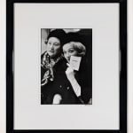 Framed black and white photograph of Marlene Dietrich sitting next to a patron holding a Chanel card at a fashion presentation at the House of Chanel