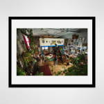 Framed photograph in black wood of an artist, Jennifer Charles, standing in the center of her loft studio adorned richly adorned with pictures and plants